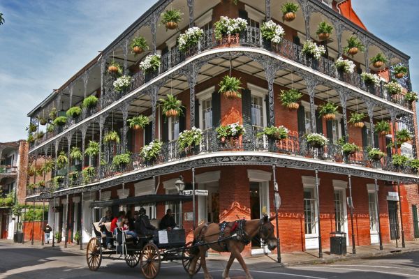 image of a New Orleans street corner, horse and buggy turning the corner and flowers on the balcony fences