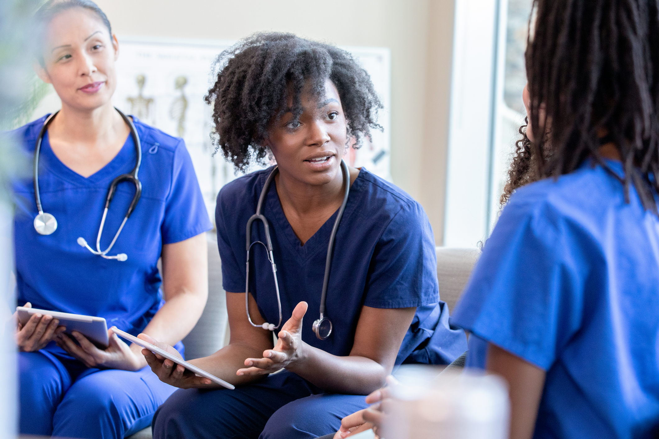 Three nursing professionals collaborate using tablets during a scholarly discussion