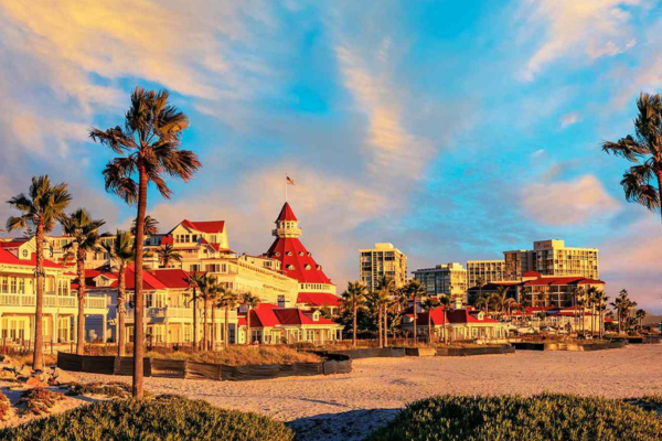 image of Hotel del Coronado with palm trees out front and a blue and pink sky image of Hotel del Coronado with palm trees out front and a blue and pink sky
